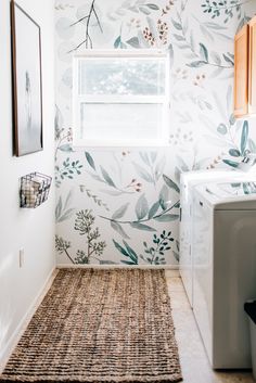 a bathroom with floral wallpaper and rug in front of the washer dryer