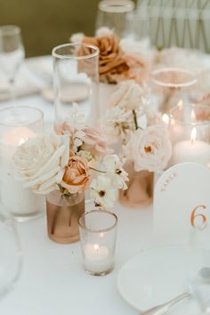 the table is set with white and pink flowers, candles, and place settings for dinner