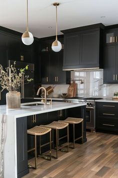 a large kitchen with black cabinets and white counter tops, gold pendant lights over the island