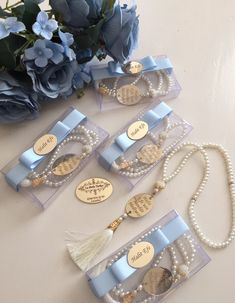 four necklaces with pearls and tassels on them sitting next to blue flowers