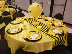 a table set up with yellow and black plates, napkins, and paper lanterns