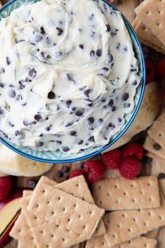 a bowl filled with white chocolate chip dip surrounded by crackers and raspberries