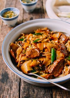 a bowl filled with noodles and meat on top of a wooden table