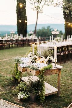 a wooden table topped with lots of flowers and greenery sitting on top of a lush green field