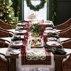 a table set for christmas dinner with holiday decorations and greenery on the windowsill