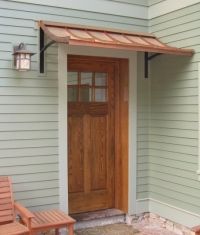 two wooden benches sitting in front of a door on the side of a house with an awning over it