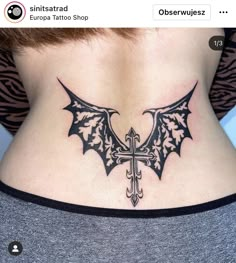 a cross and bat tattoo on the back of a woman's lower back neck