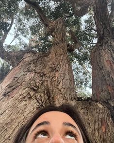 a woman standing in front of a tree looking up at the sky with her eyes wide open