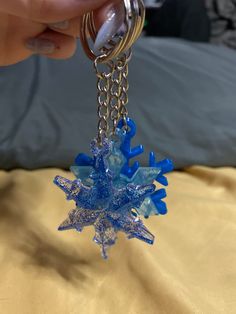 a hand holding a blue and silver snowflake keychain on a bed