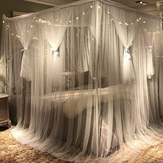 a canopy bed with white curtains and lights