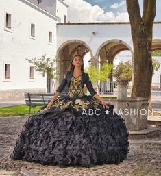 a woman in a black and gold dress sitting on a bench next to a tree