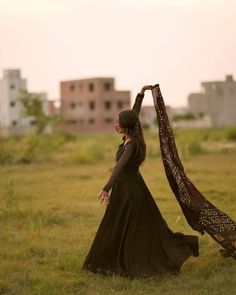 a woman in a long black dress is walking through the grass with her shaw around her neck