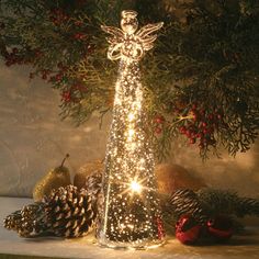 a lighted christmas tree with angel figurine and pine cones in front of it