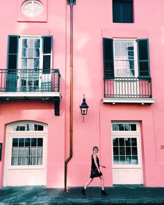 a woman walking down the street in front of a pink building with black shutters