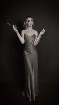 a woman in a long silver dress holding a wand and wearing gloves with tattoos on her arms