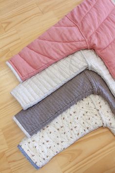 four quilts laid out on top of each other in different colors and sizes, laying on a wood floor