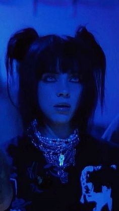 a woman with black hair wearing a necklace and piercings in the dark blue light