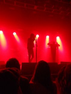 two people on stage with red lights and microphones in front of them, while the audience looks on