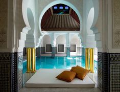 an indoor swimming pool with white walls and yellow pillows on the bottom, surrounded by arches