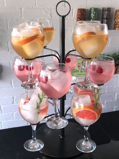 several glasses filled with different types of drinks on top of a black table next to a white brick wall