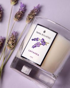 a candle and some flowers on a purple surface with lavenders in the foreground