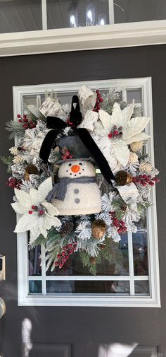 a wreath with a snowman on it hanging from the side of a house door