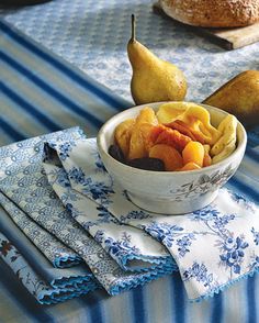 a bowl filled with fruit sitting on top of a blue and white cloth covered table