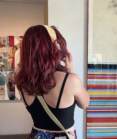 a woman with red hair wearing a black tank top and floral print skirt standing in front of art work