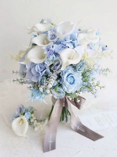 a bridal bouquet with blue flowers and white calla lilies on a lace tablecloth