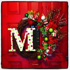 a wreath with the letter m on it is hanging on a red door and decorated with ornaments