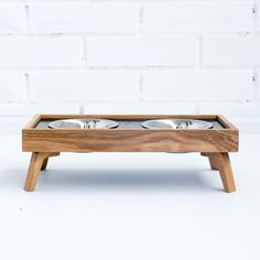 a wooden tray with three bowls in it on a white table next to a brick wall