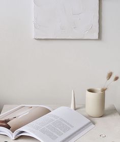 an open book sitting on top of a table next to a cup and vase filled with flowers