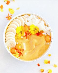 a bowl filled with bananas, oranges and other fruits on top of flowers next to petals