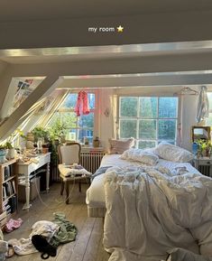 an attic bedroom with white bedding and lots of clutter on the floor,