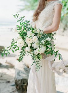 a woman in a wedding dress holding a bridal bouquet with white flowers and greenery