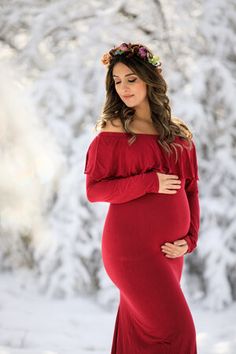 a pregnant woman wearing a red dress in the snow with her hands on her stomach