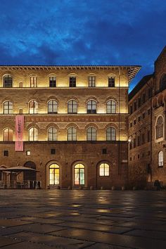 an old building lit up at night with lights on the windows and cobblestone floor