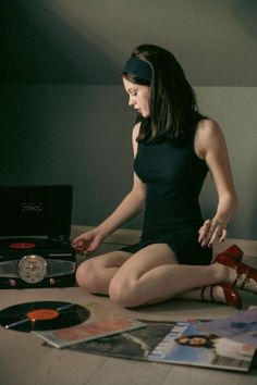 a woman sitting on top of a bed next to record player and cd's