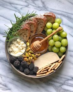 a platter with bread, grapes, crackers and honey on it is sitting on a marble surface