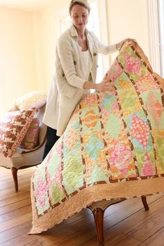 a woman holding up a quilt on top of a bed