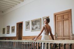 a woman standing on top of a balcony next to a wooden railing with pictures on the wall behind her