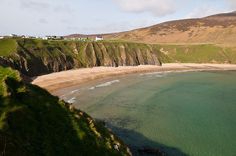 an ocean view with houses on the cliff and green grass in the foreground, near a sandy beach