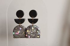 a pair of black and white earrings with silver glitters hanging from it's sides