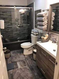 a bathroom with gray tile and wooden cabinets, toilet, sink, and shower stall