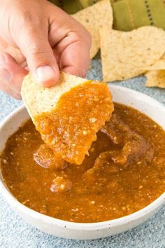 a person dipping tortilla chips into a bowl of salsa