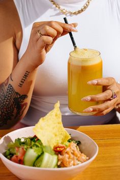 a woman holding a drink in her right hand while sitting at a table with food