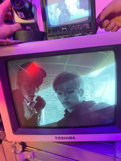 a television with two people on it in front of a purple light and a camera