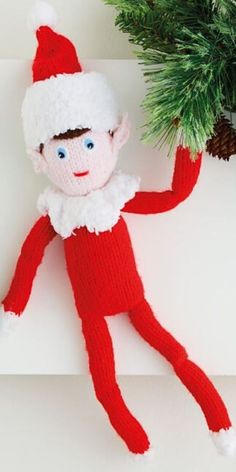 a knitted elf doll sitting next to a christmas tree on top of a shelf