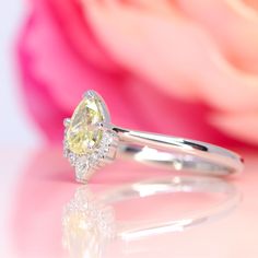 a yellow diamond ring sitting on top of a white surface next to a pink rose