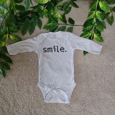 a long sleeved bodysuit with the word smile printed on it sitting next to some green leaves